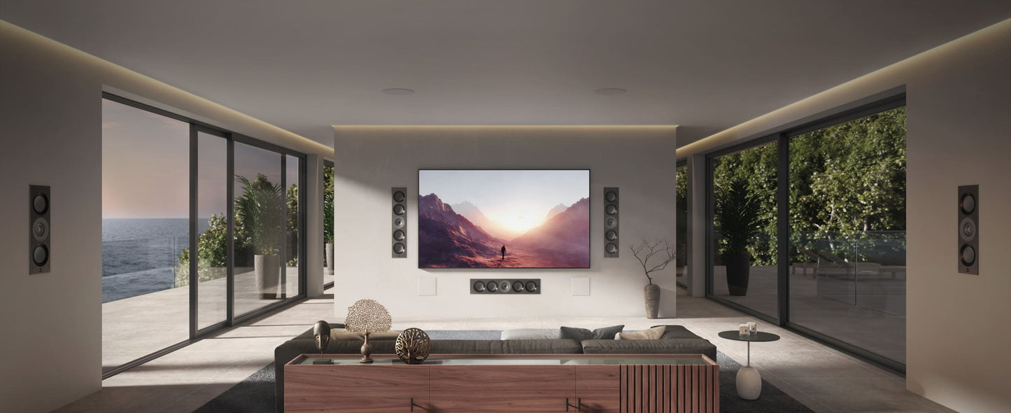 Modern living room with a large TV displaying a mountain scene with KEF Ci5160REFM-THX Reference In-Wall speakers installed, surrounded by large windows with a view of the ocean.