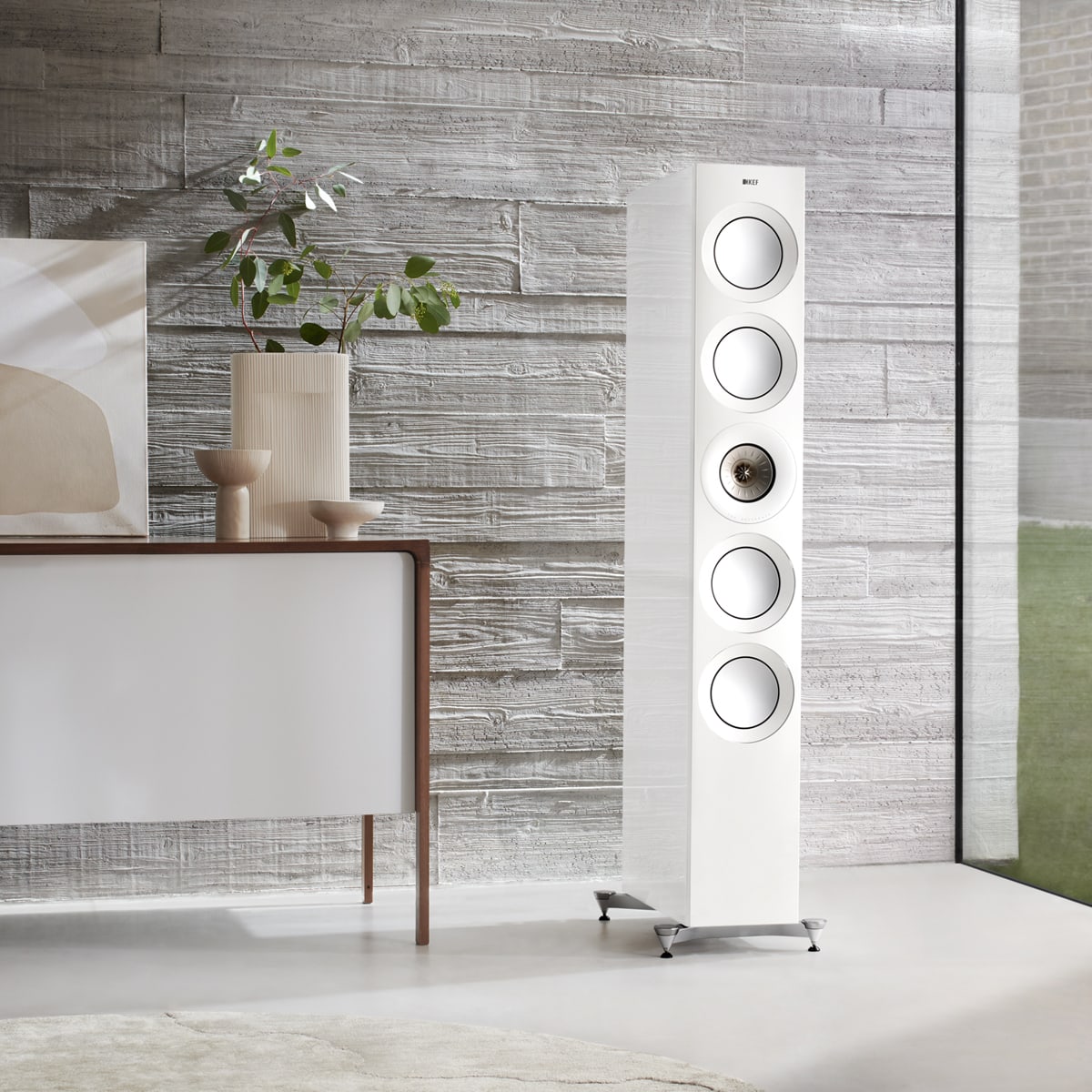Tall white KEF Reference 2 Meta speaker against a textured wall with decorative elements