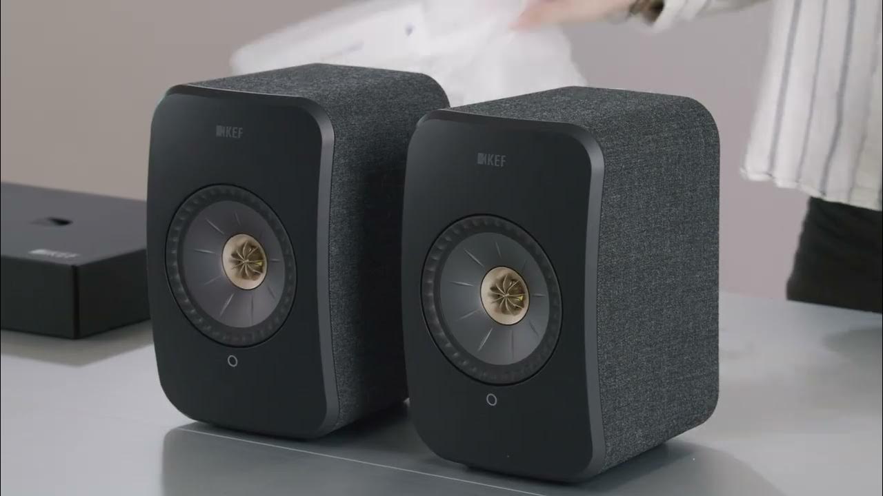 Two carbon black KEF LSX II Wireless Speakers on a surface with a blurred background