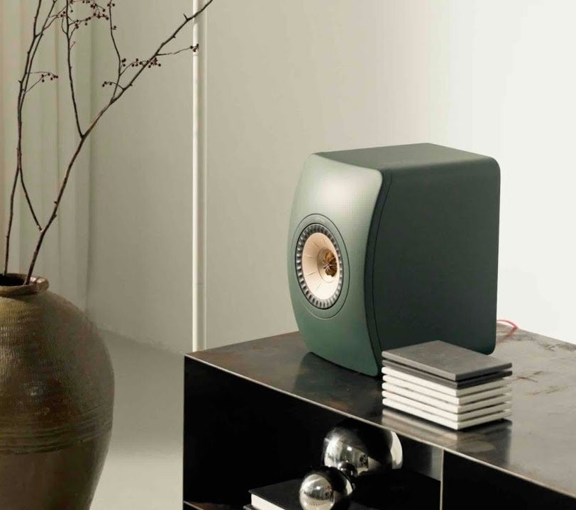 Modern moss green KEF LS50META Bookshellf Monitor on a dark surface with a neutral background.