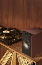 Burgundy KEF Coda W Powered Speaker on a wooden surface with a vinyl record player and records in the background.