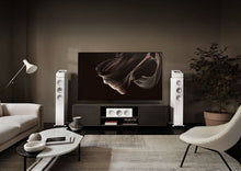 Modern living room with a large TV on a stand, flanked by KEF R7 Meta Floor Standing Speaker, in a dimly lit room.