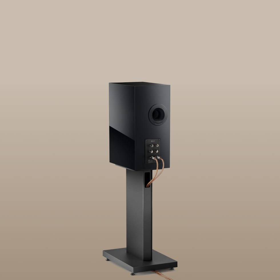 Back side of a black KEF speaker on a KEF S3 Floor Stand for R3 against a beige background