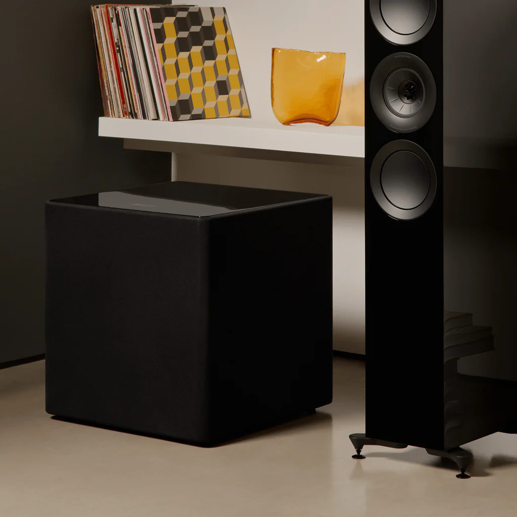 Black KEF KUBE 15 MIE 15" Subwoofer and tall floor-standing speaker in a room setting.