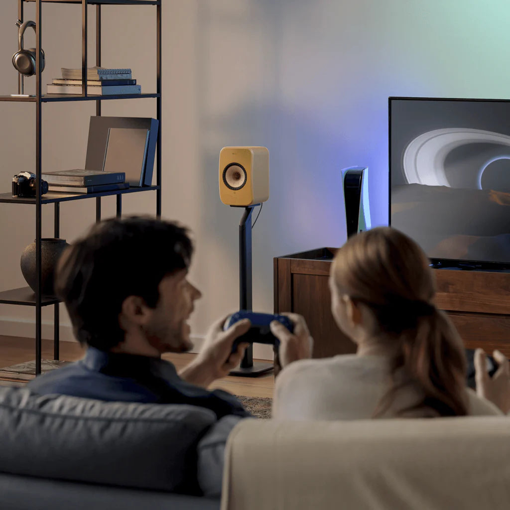 Two people playing video games in a living room with a TV and KEF LSX II Wireless Speakers.