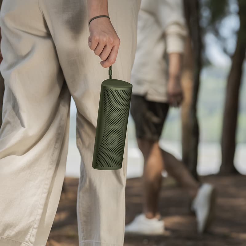 Person holding a green KEF MUO Portable Bluetooth Speaker outdoors with blurred background