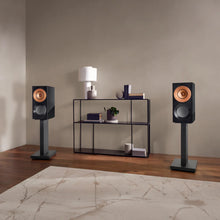Pair of KEF Reference 1 Meta speakers on stands in a room with a shelf and decor items.