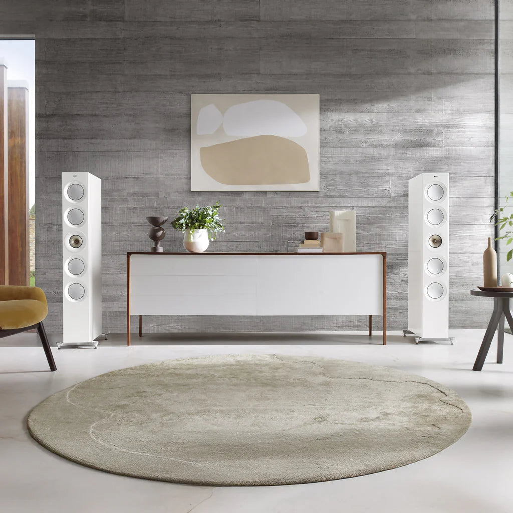 Modern living room with white furniture, KEF Reference 5 Meta speaker, round rug, and abstract wall art.