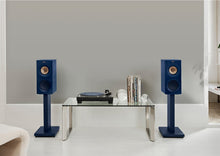 Blue KEF speakers on KEF S3 Floor Stands for R3 with a turntable and records on a glass table against a gray wall.