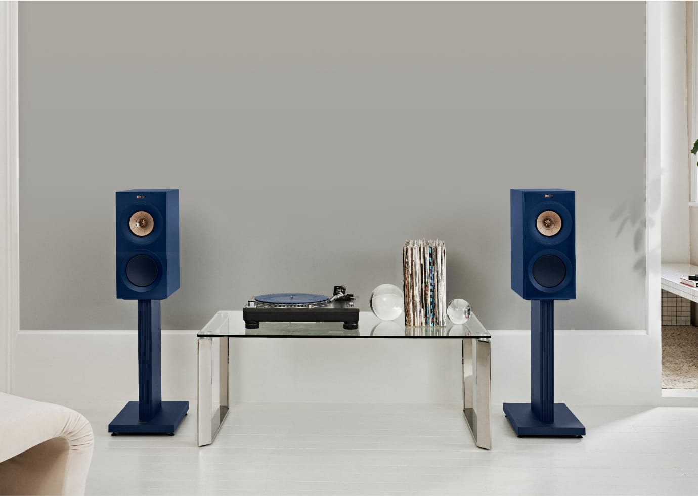 Blue KEF speakers on KEF S3 Floor Stands for R3 with a turntable and records on a glass table against a gray wall.