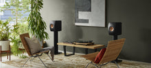 Modern living room with two speakers on KEF S2 Floor Stands for LS Series, a coffee table, and decorative items.
