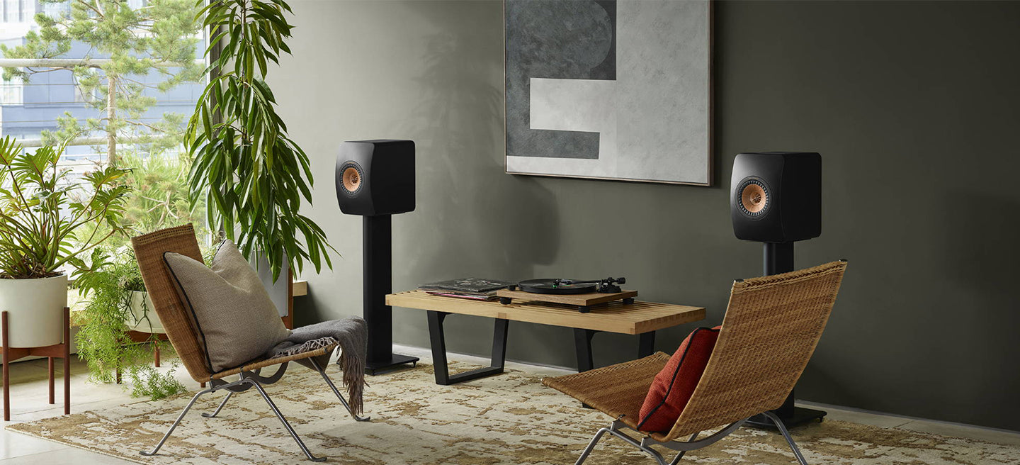 Modern living room with two speakers on KEF S2 Floor Stands for LS Series, a coffee table, and decorative items.