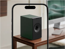 Green KEF Coda W Powered Speaker on a wooden table with a phone showing its reflection